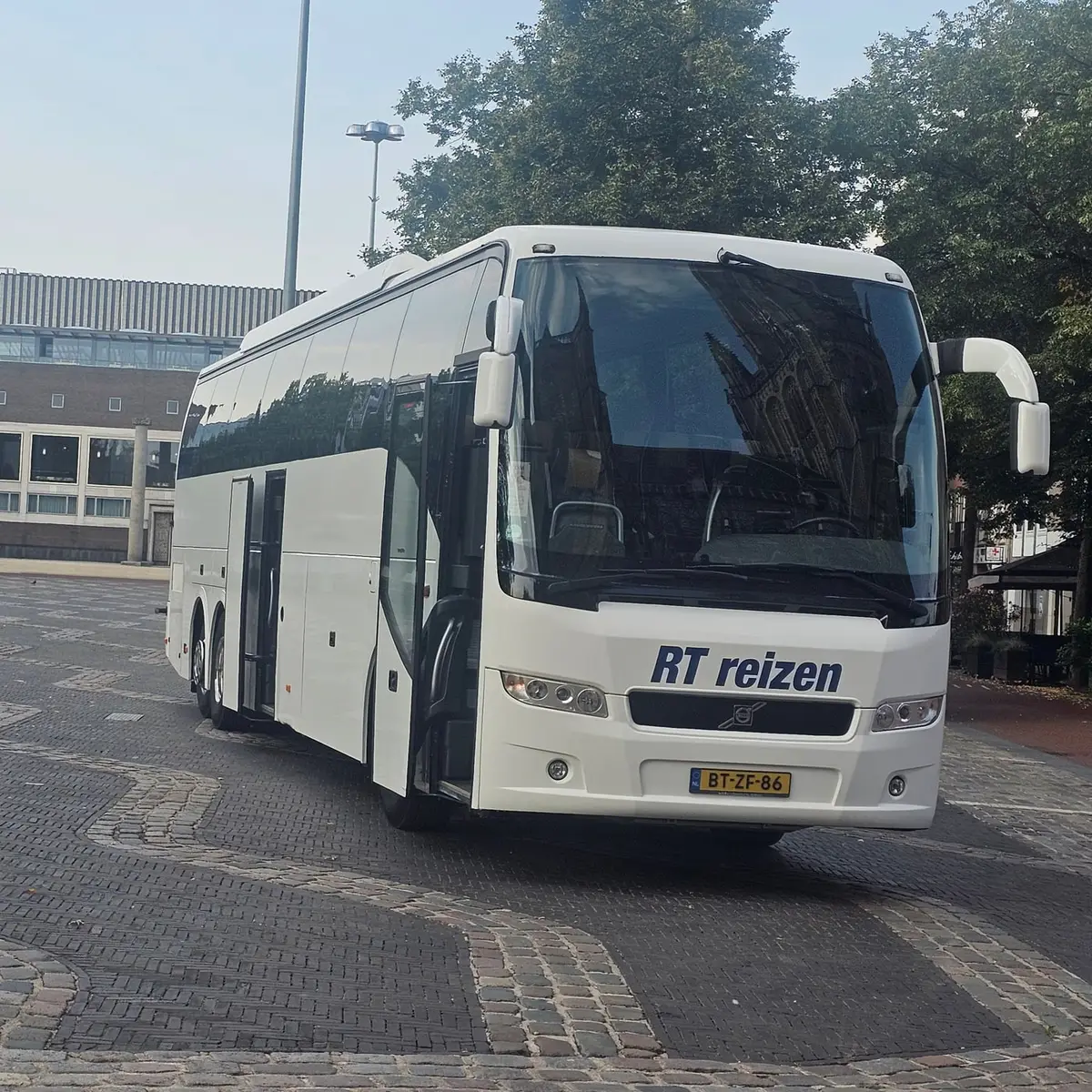 Touringcar van RT Reizen staat in ochtendlicht op een plein met klinkers in Arnhem, met de hele bus in beeld.