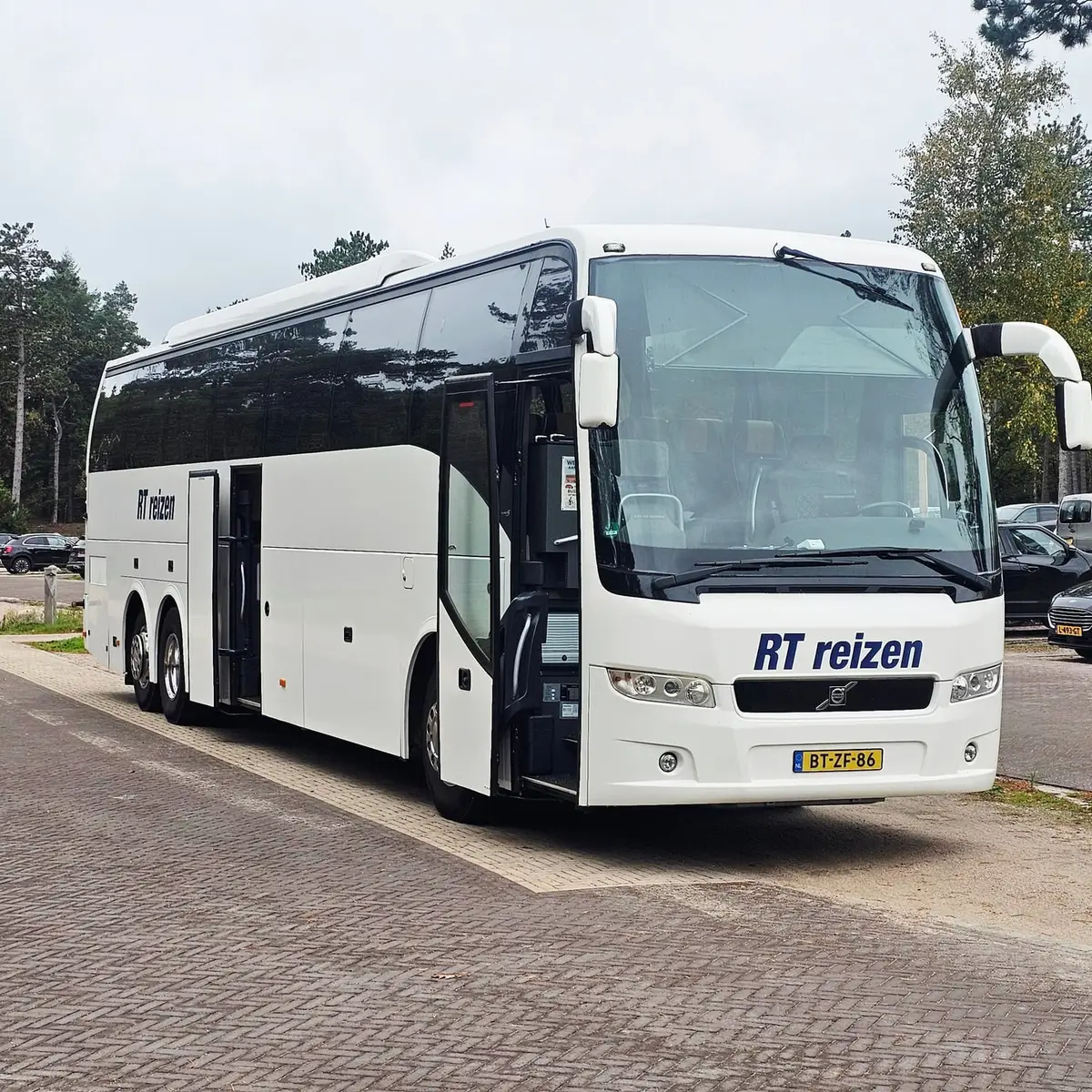 Touringcar van RT Reizen met de deur open op een parkeerplaats aan een bosrand, met de hele bus in beeld.