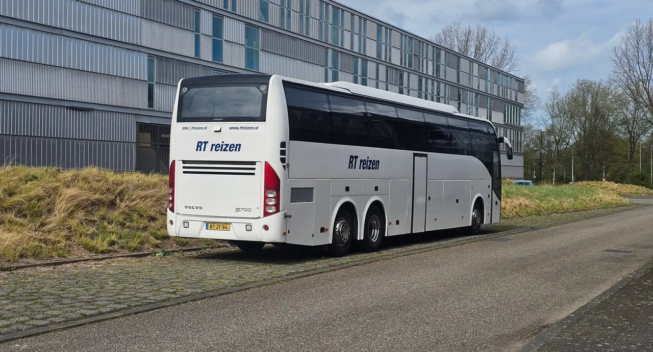 Touringcar van RT Reizen staat langs de weg met de berm ernaast, klaar om een groep op te halen.