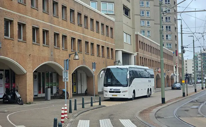 Touringcar van RT Reizen in een stadsstraat met tramrails, langs een gebouw met arcades.