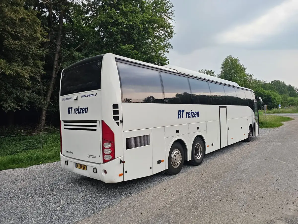 De touringcar van RT Reizen op een landweg tussen het groen.
