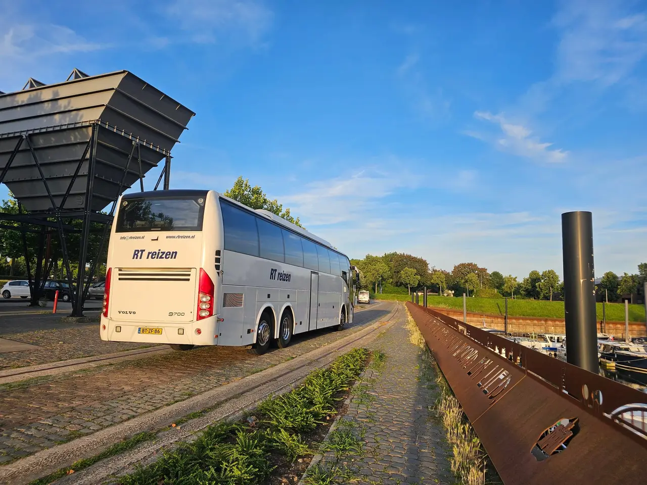 Touringcar van RT Reizen op de kade in Doesburg, met de haven en de aangemeerde boten ernaast.