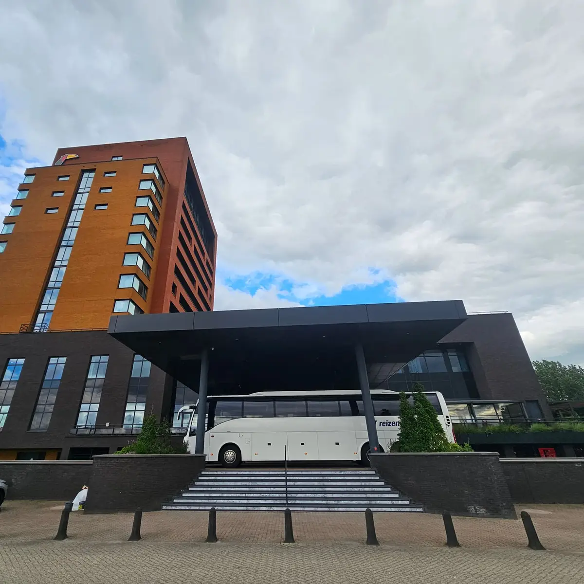 Touringcar van RT Reizen onder de luifel bij Van der Valk Duiven, met de hoteltoren erachter.