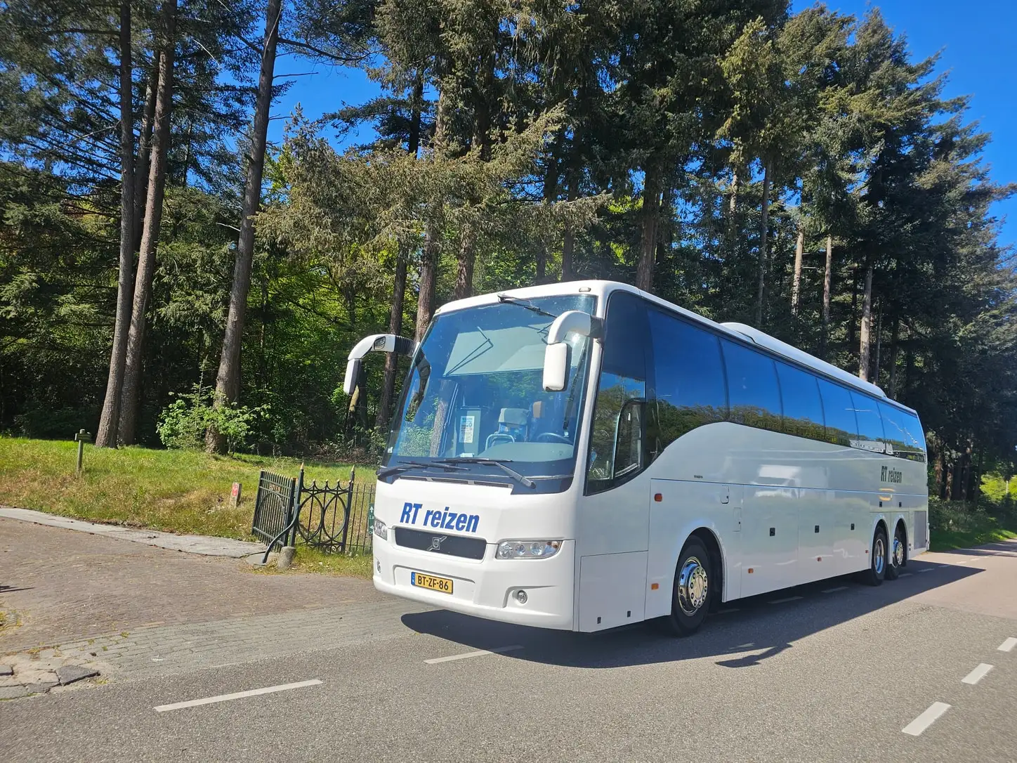 Touringcar van RT Reizen onderweg op een bosweg, driekwart van voren gezien.