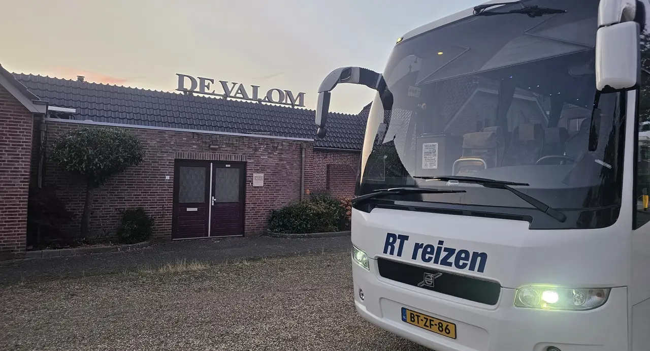 Touringcar van RT Reizen staat bij het invallen van de avond klaar voor partycentrum De Valom in Huissen, met de naam op de gevel.