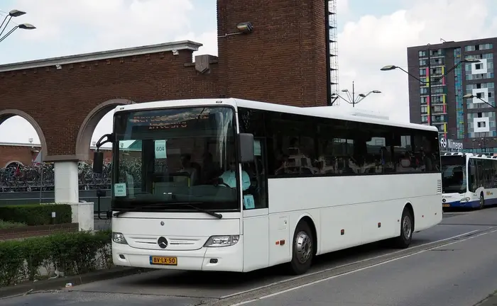 Bus van RT Reizen rijdt door een stadsstraat langs een gebouw met arcades.