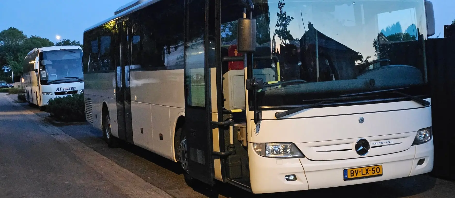 Twee bussen van RT Reizen achter elkaar langs de weg, in de schemering.
