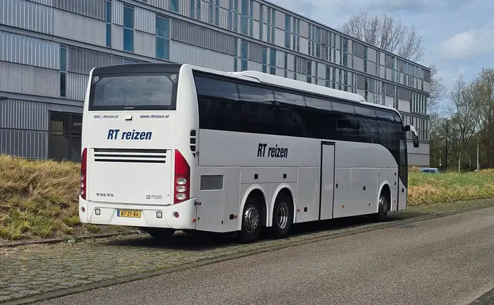 Touringcar van RT Reizen, geparkeerd langs de weg bij een groot modern gebouw.
