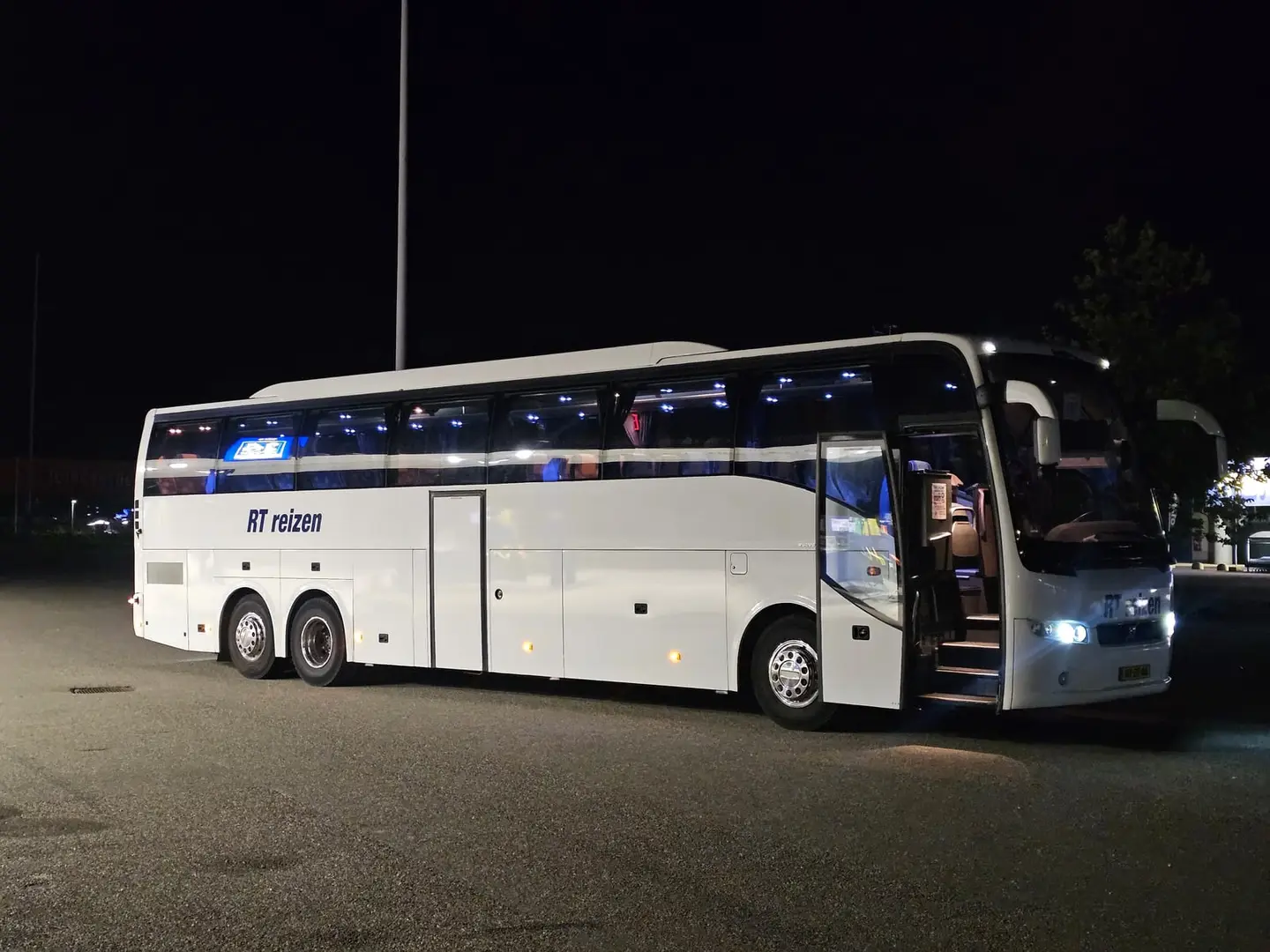 Touringcar van RT Reizen met de deur open en de sfeerverlichting aan, klaar om in te stappen.