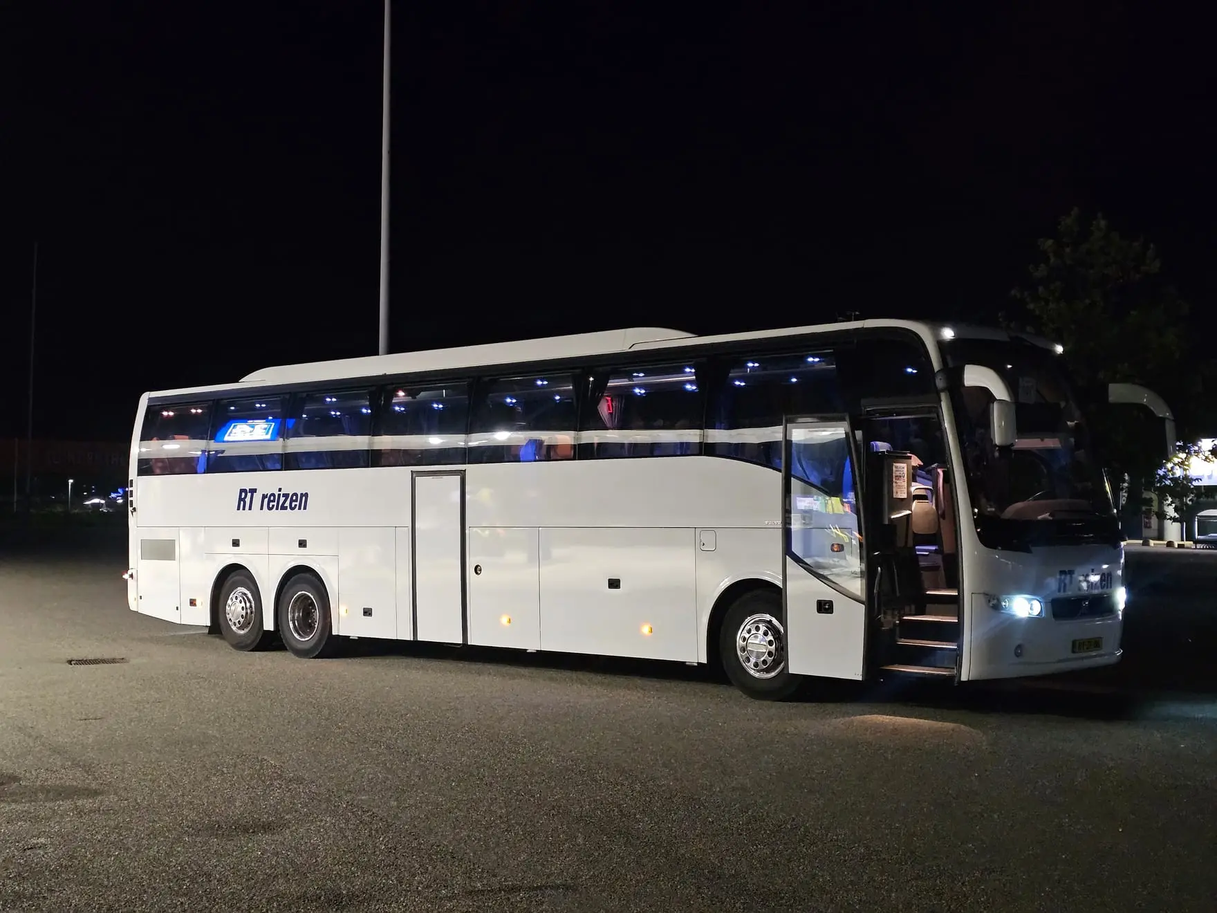 Touringcar van RT Reizen in het donker, met de deur open en de verlichting aan