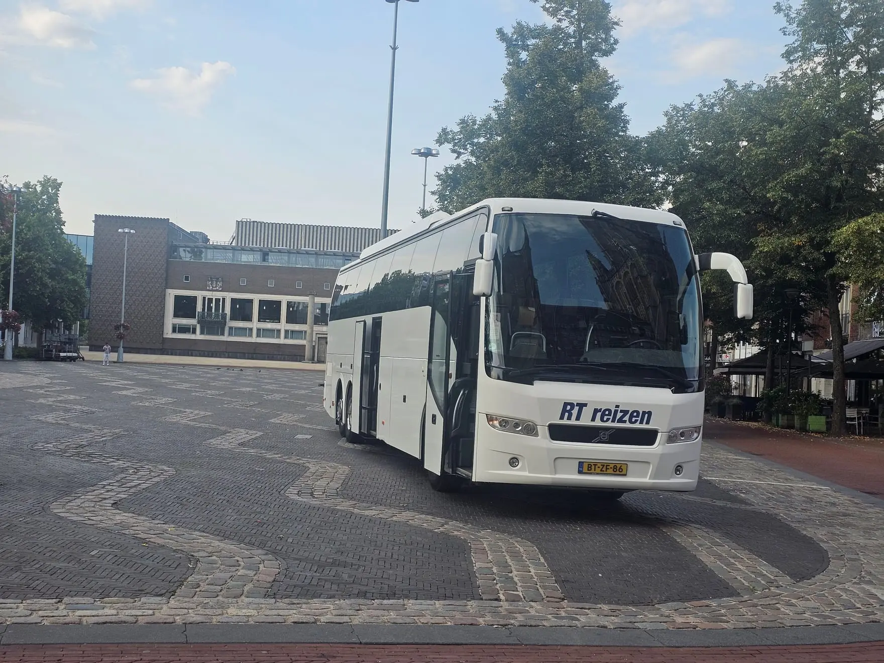 Touringcar van RT Reizen op een plein voor een gebouw, in de ochtend