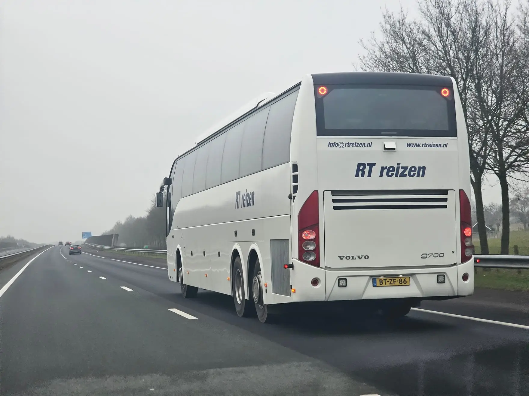 Touringcar van RT Reizen onderweg op de snelweg op een grijze winterdag, met kale bomen langs de weg